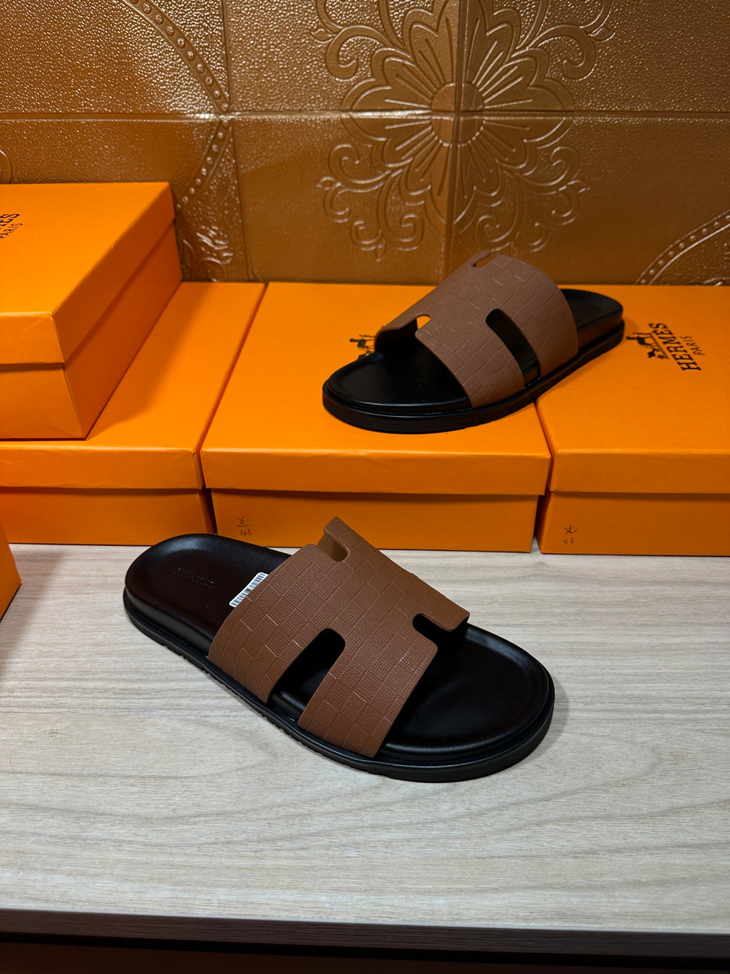Hermes slide sandals with tan leather strap and black rubber sole, pair on floor
