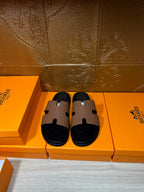 Hermes slide sandals with tan leather strap and black footbed, side-by-side view