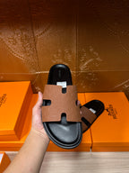 Hermes slide sandal close-up held in hand, tan strap with black footbed