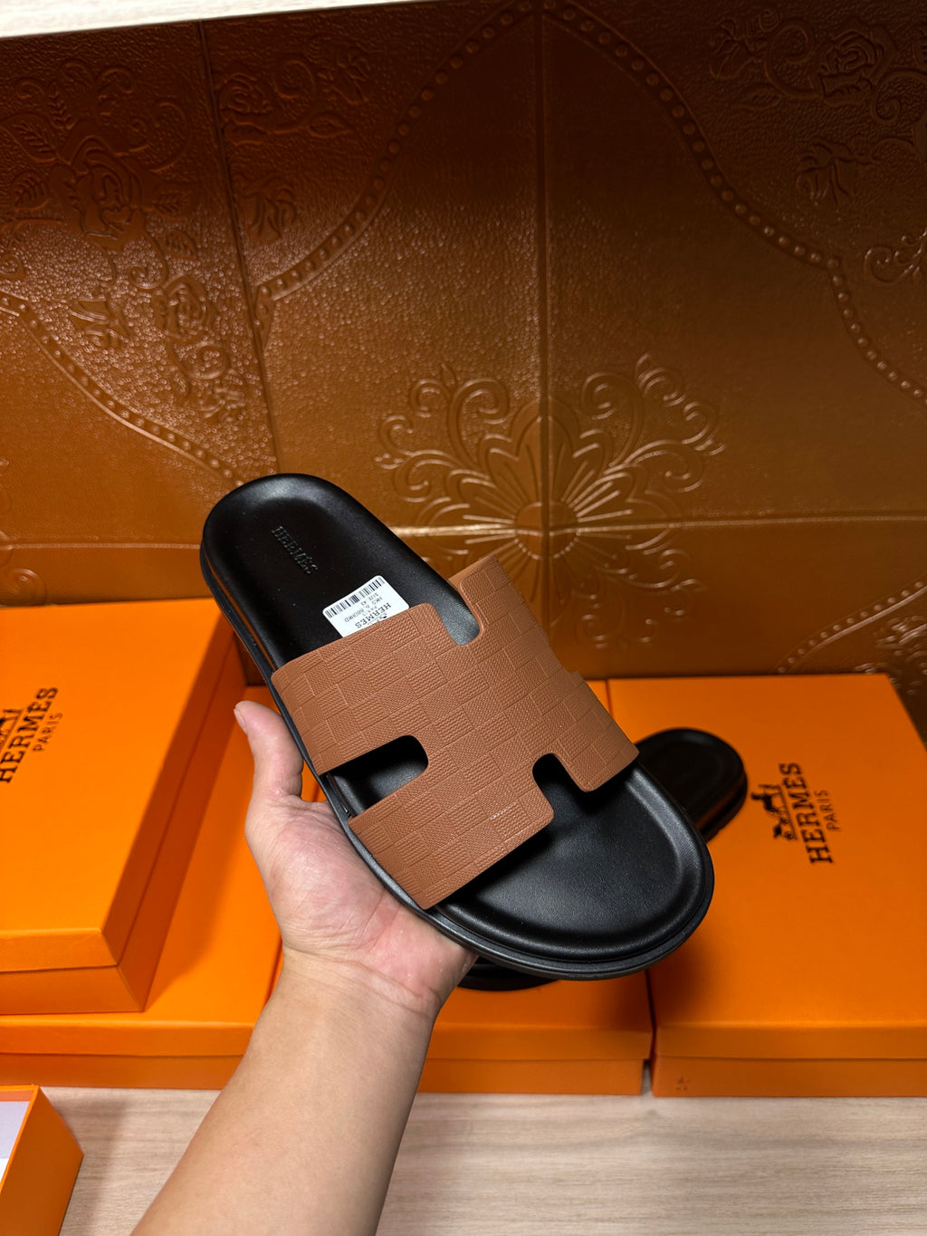 Hermes slide sandal held in hand: tan leather strap over black footbed