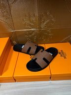 Hermes slide sandals: tan leather strap with cutout detail over black sole, angled