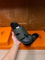 Hermes black slide sandal held in hand, textured wide strap and flat sole