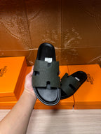 Hermes black slide sandal held up, wide textured strap and open toe