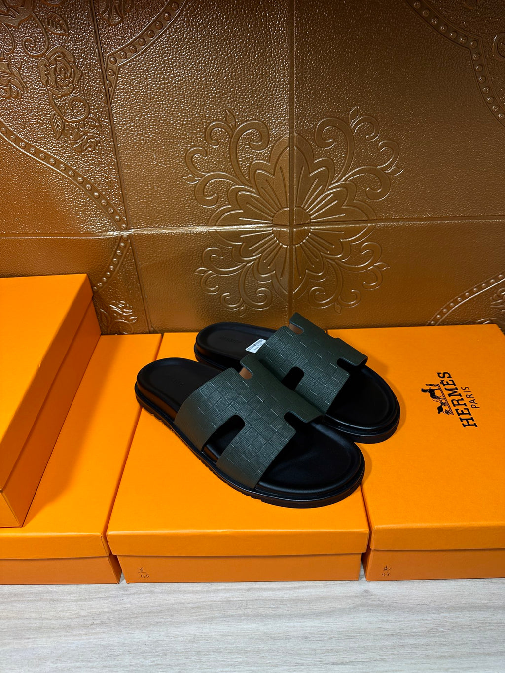 Hermes black slide sandals resting on boxes, wide strap and flat rubber sole