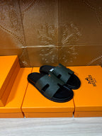 Hermes black slide sandals resting on boxes, wide strap and flat rubber sole