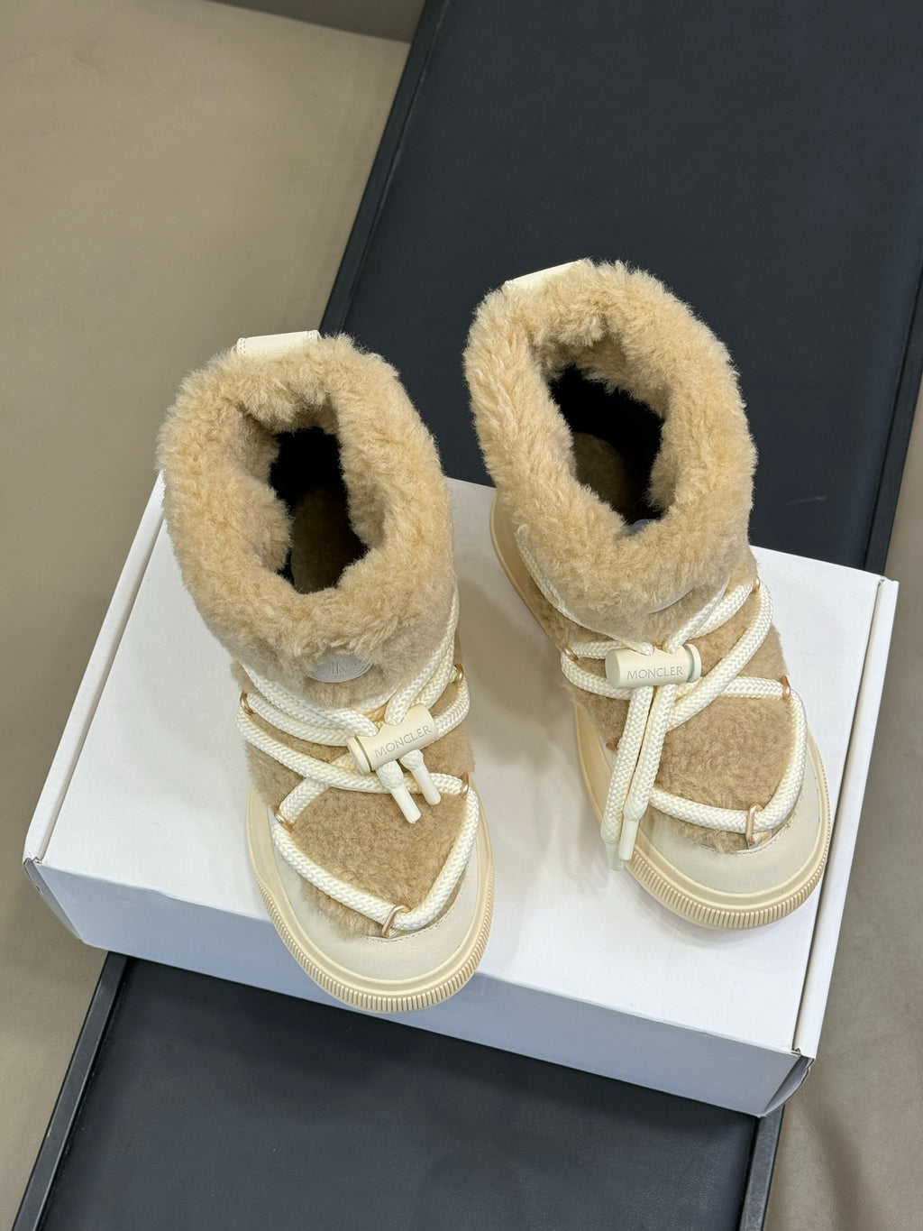 Moncler lace-up shearling boots in light tan, shown side by side on a box