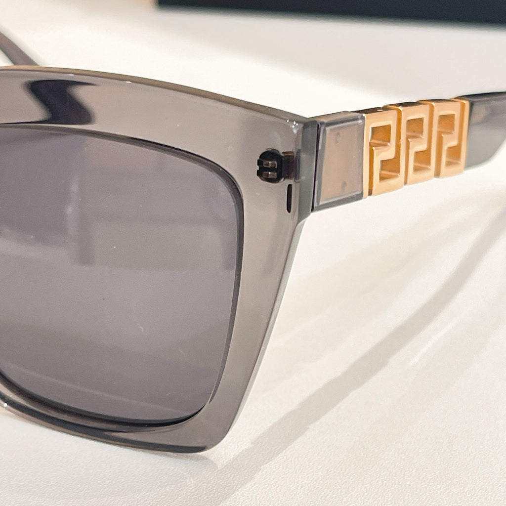 Clear gray sunglasses temple with gold geometric logo detail