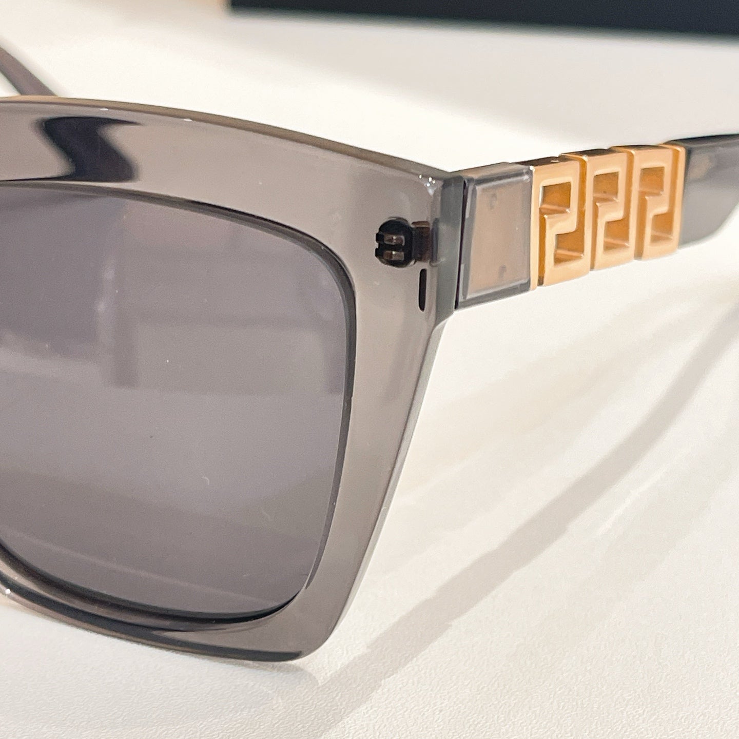 Clear gray sunglasses temple with gold geometric logo detail