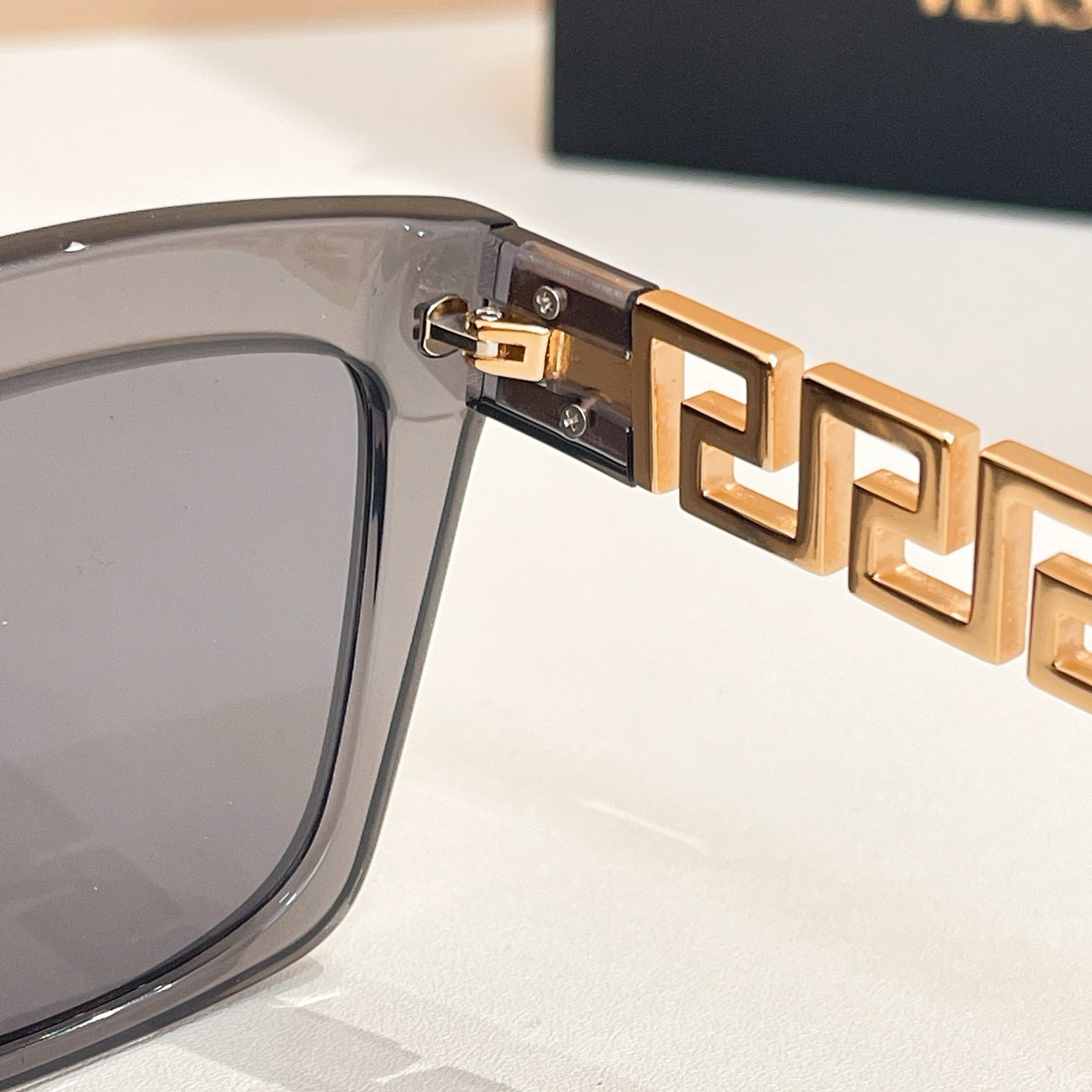 Gold logo hinge detail on clear gray sunglasses frame