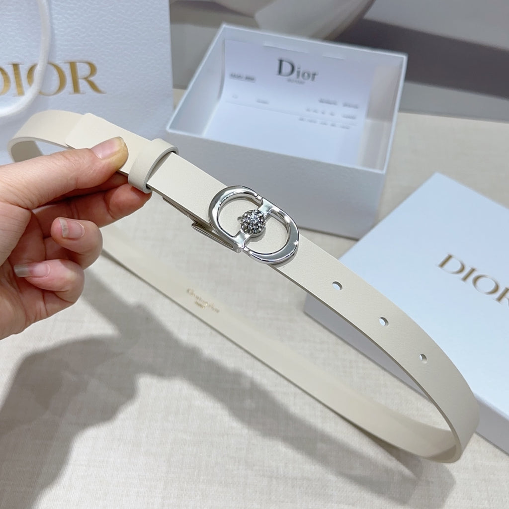 Light leather belt held in hand, featuring a silver oval buckle with crystal center