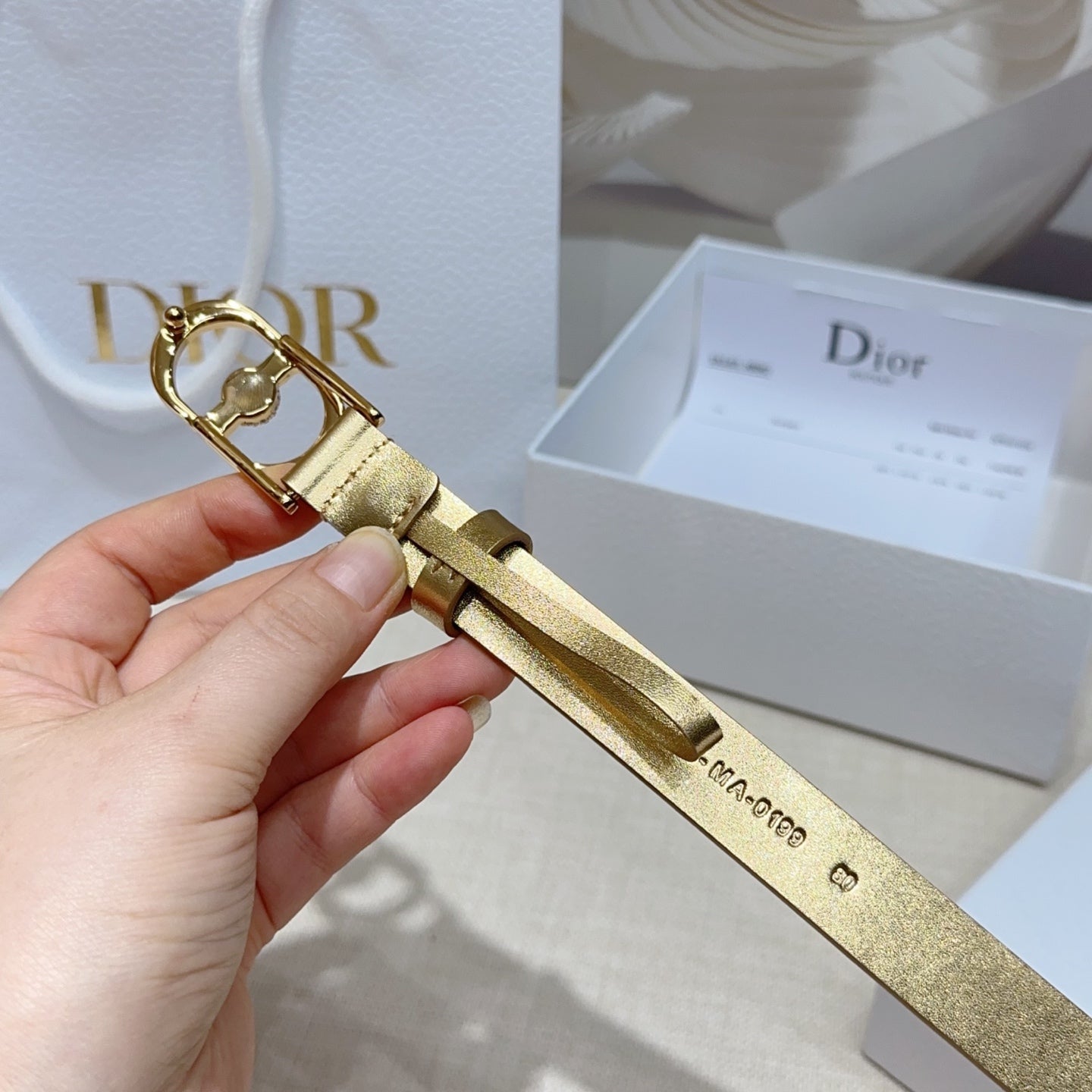 Dior gold-tone belt end view with oval buckle and embossed maker marks on strap