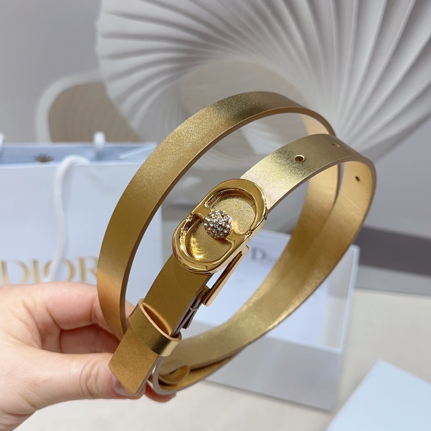 Dior gold-tone belt looped in hand, oval buckle with round rhinestone centerpiece