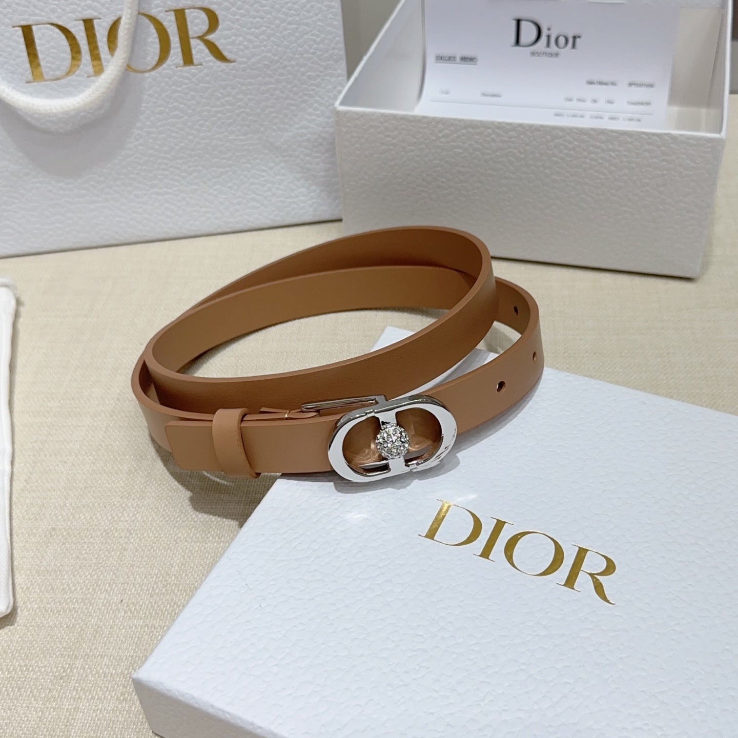 Tan leather belt with silver buckle featuring a round jeweled clasp