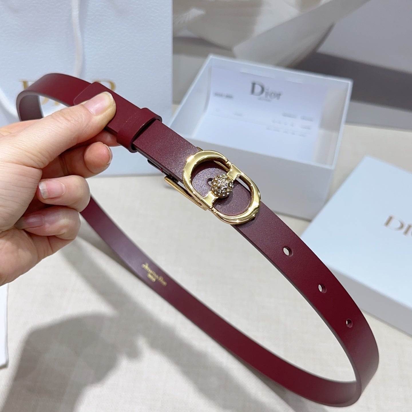 Burgundy leather belt with gold-tone buckle, crystal charm, and punched holes