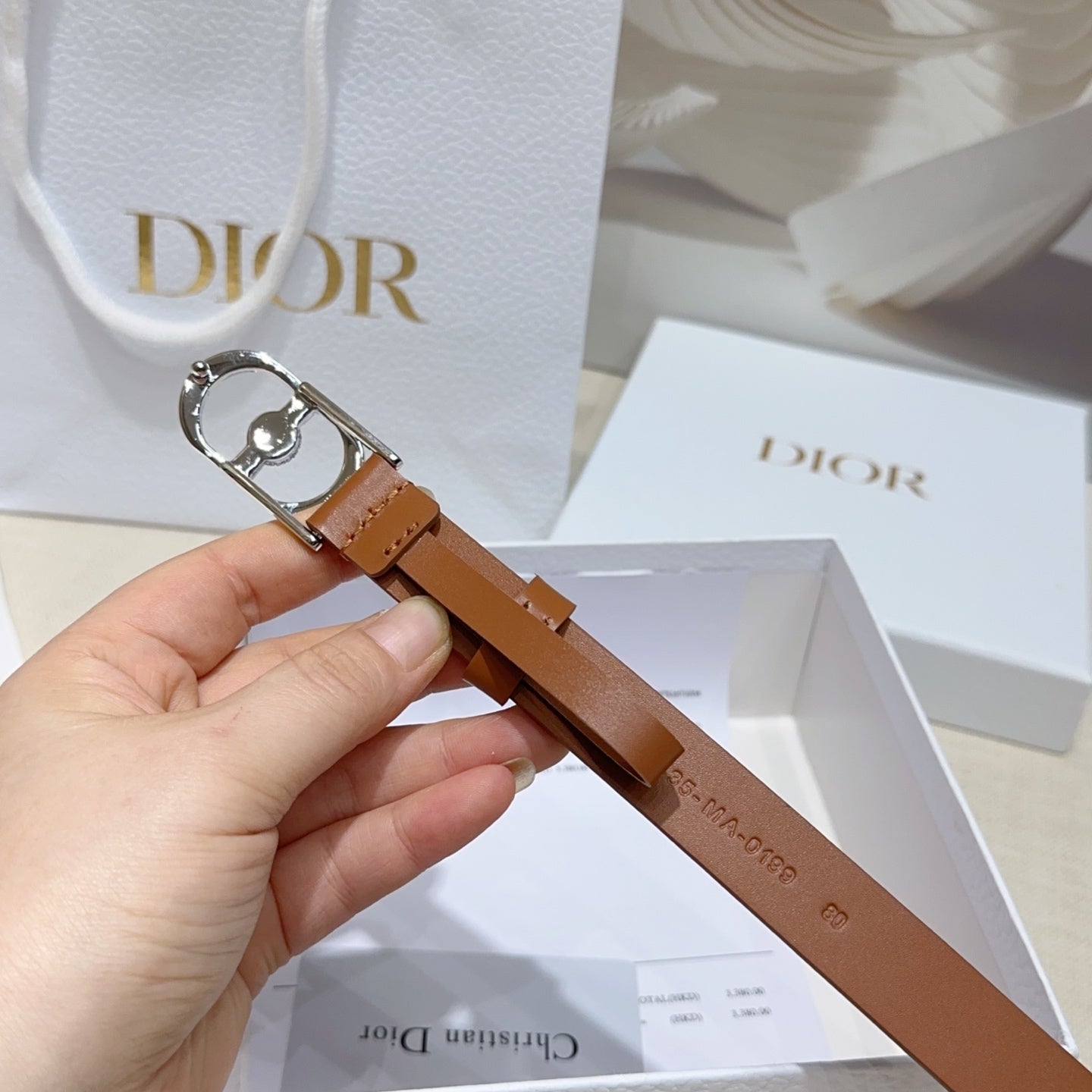 Tan leather belt with silver buckle and crystal charm, held in hand