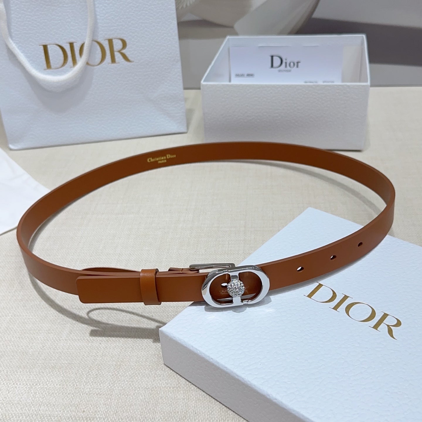 Tan leather belt with silver buckle and oval crystal detail, flat lay