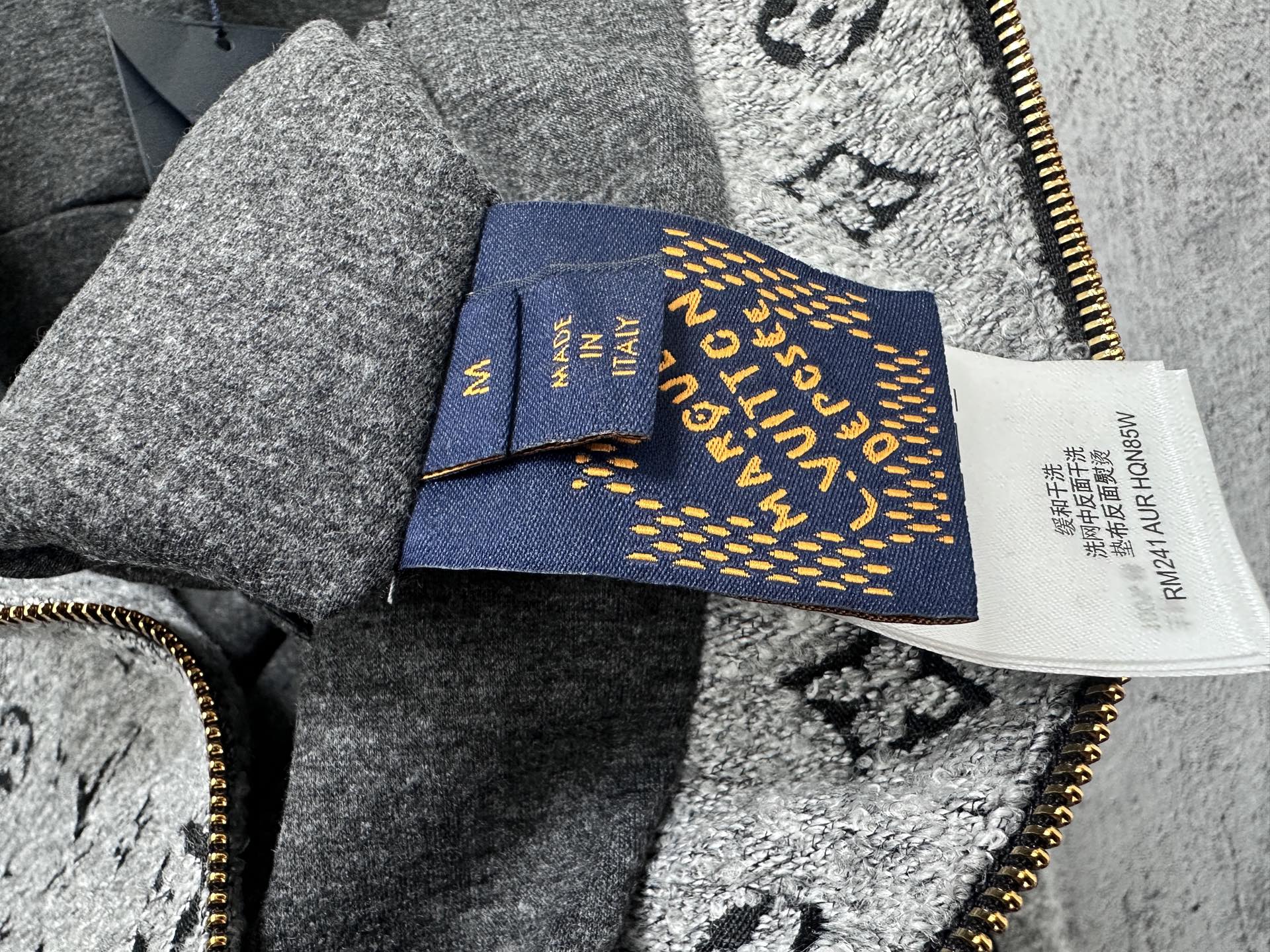 Louis Vuitton hooded jacket interior tag and blue label near zipper, on gray fabric