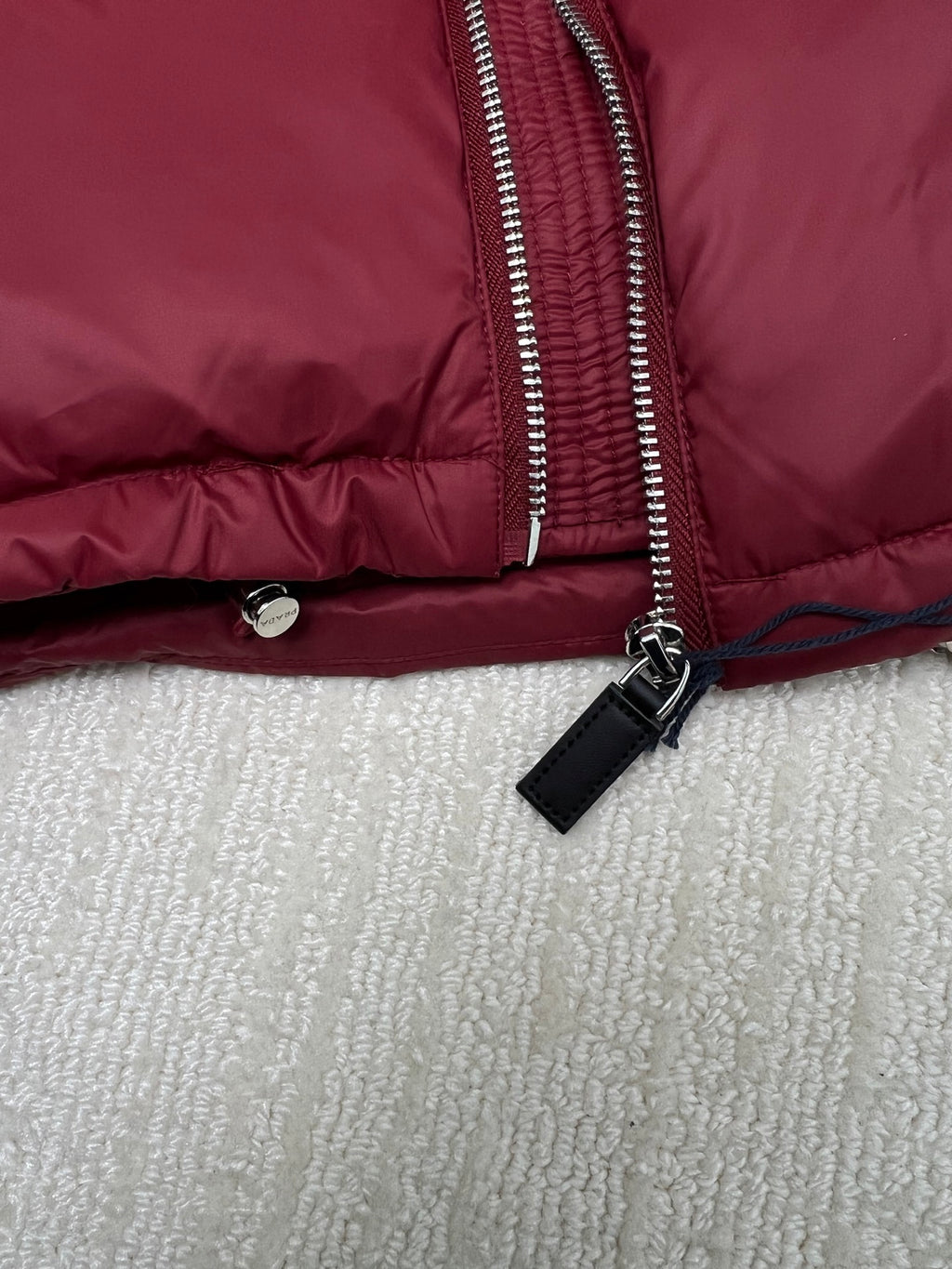 Long padded jacket detail: silver zip, black tag pull, snap waist button