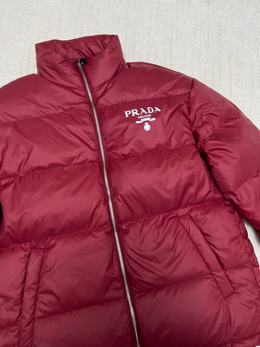 Prada red puffer jacket with stand collar, front zipper, and PRADA logo