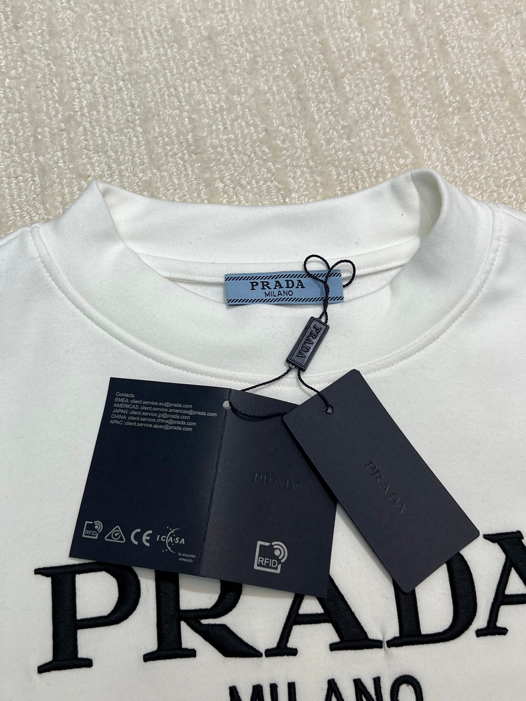 White crewneck shirt with PRADA logo at chest and attached hang tag