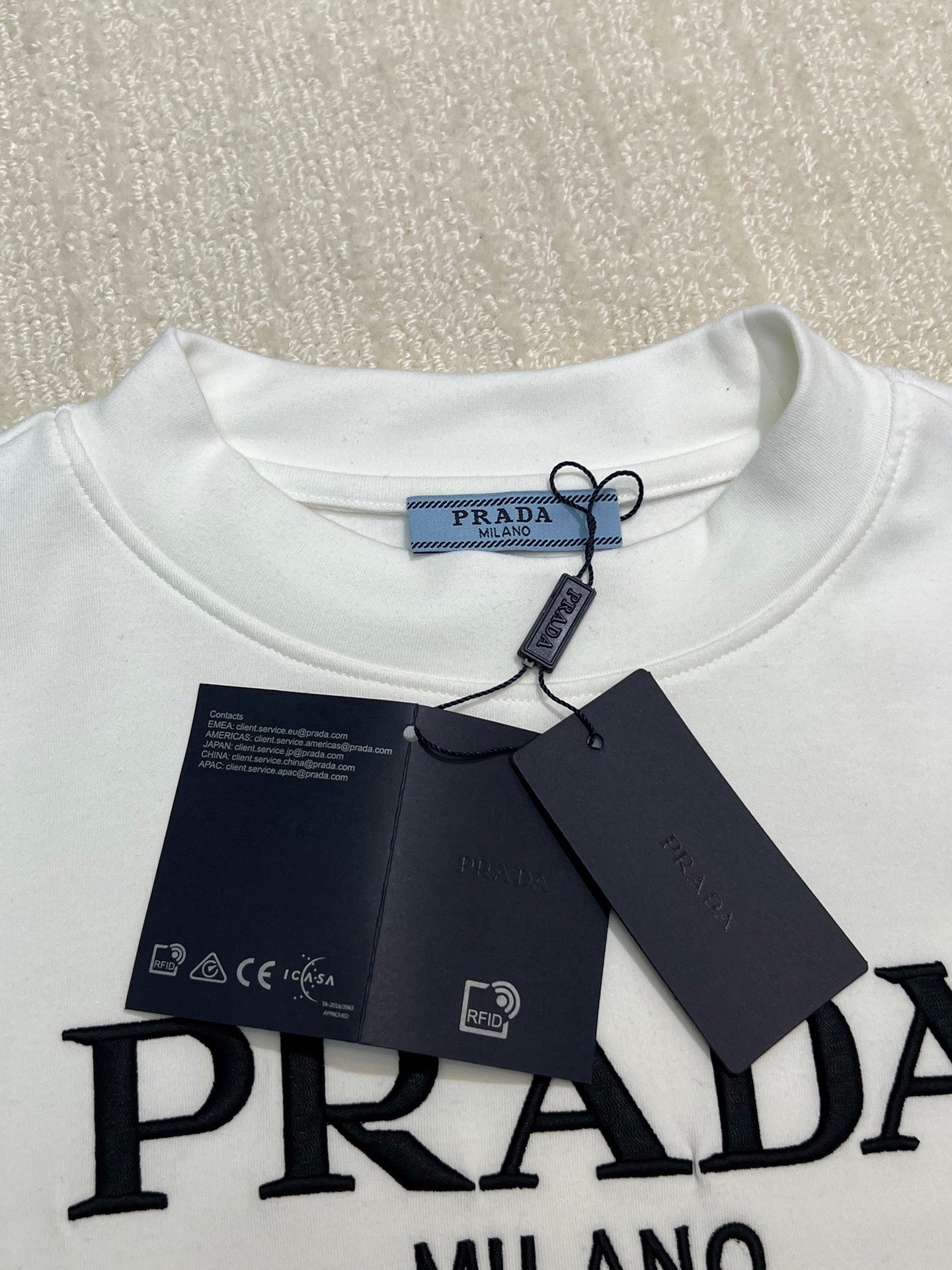 White crewneck shirt with PRADA logo at chest and attached hang tag