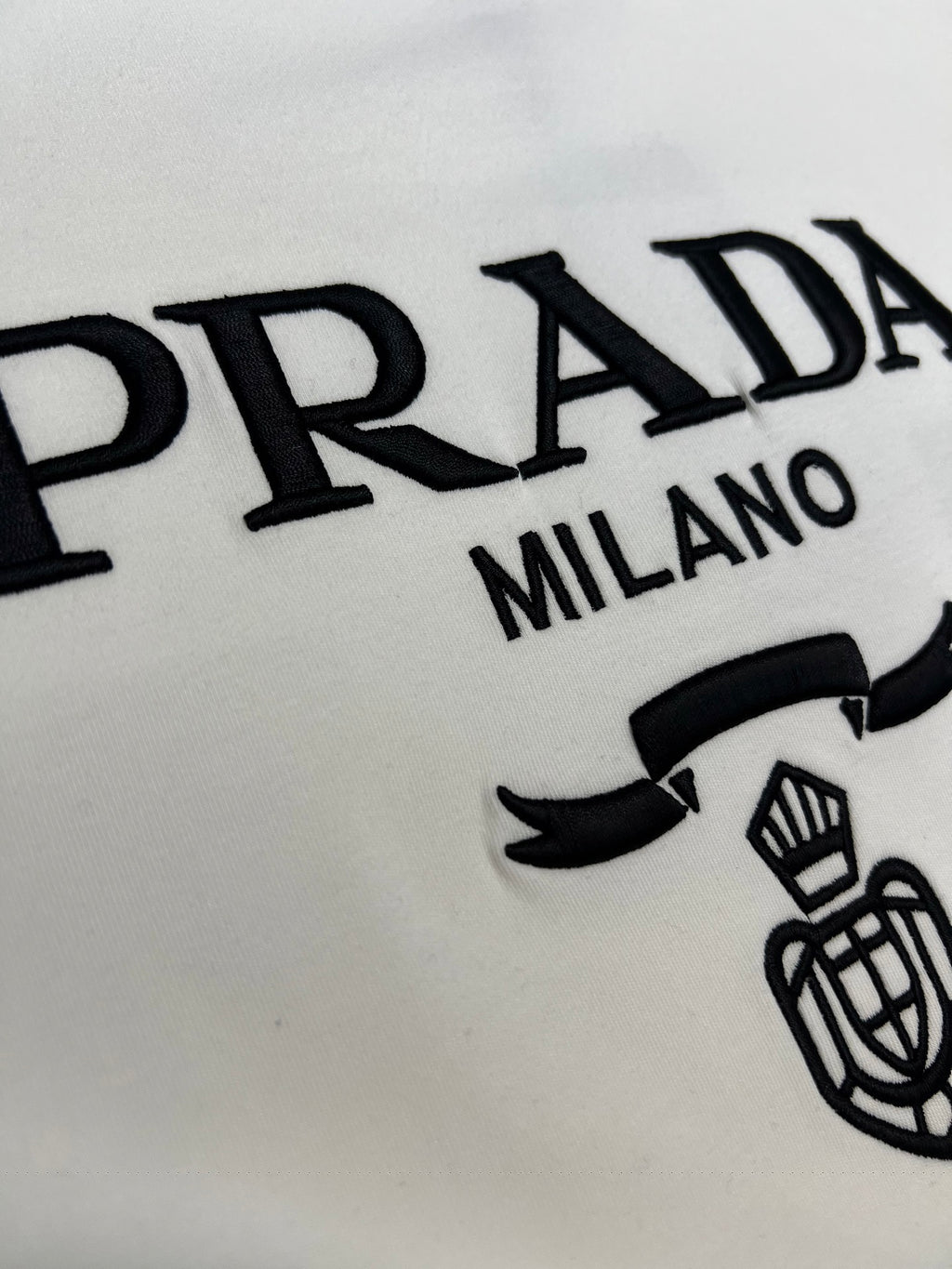 White long-sleeve shirt detail with PRADA MILANO lettering and crest