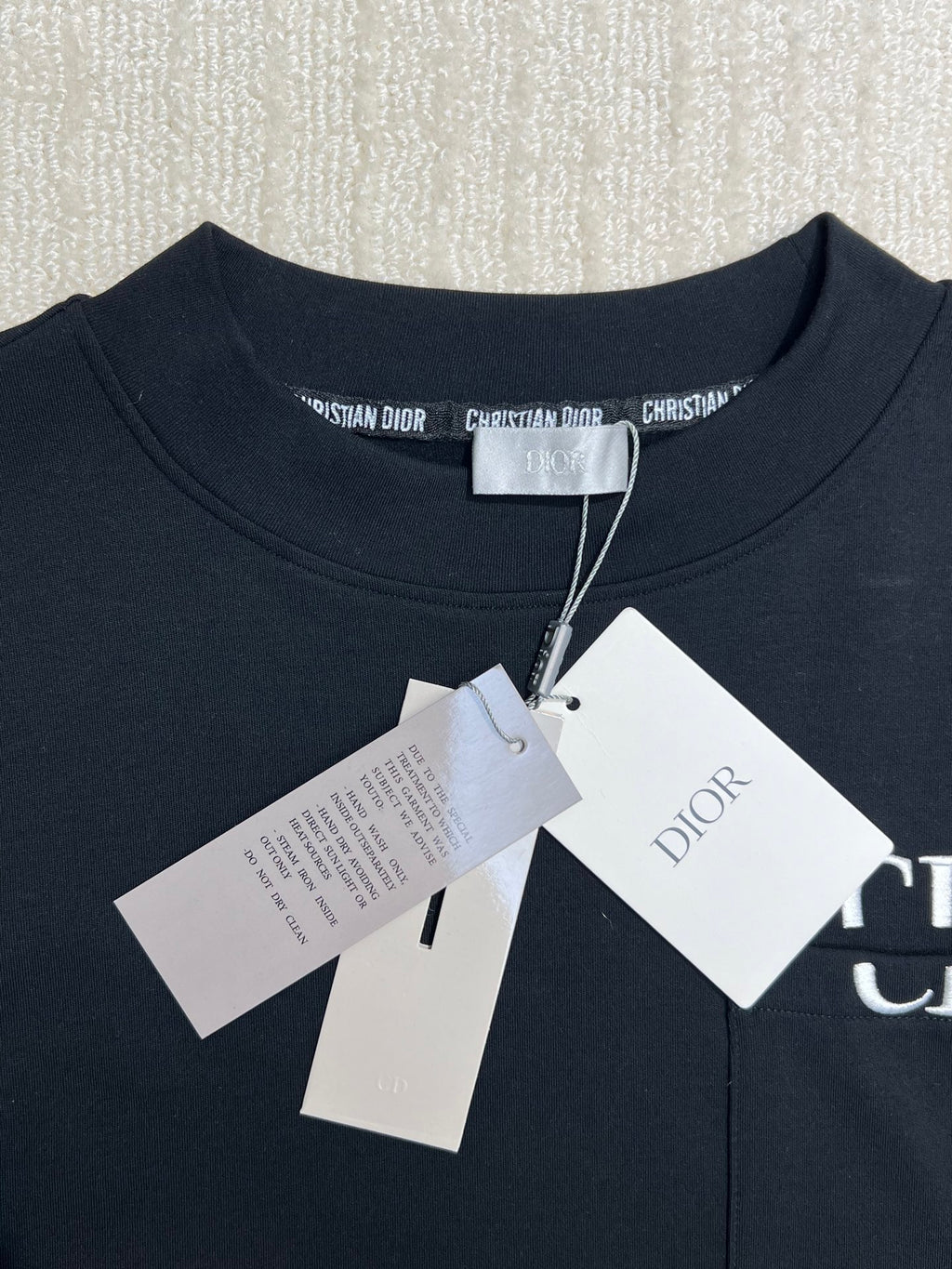 Dark crewneck sweatshirt with brand neck label and attached white tag pack