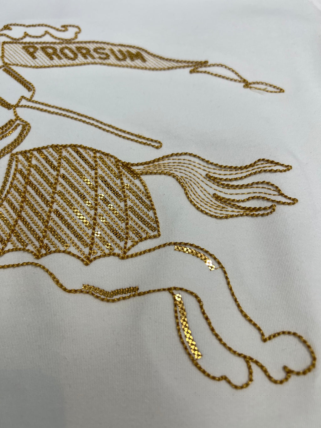 Close-up of gold embroidered horse graphic on a white long-sleeve shirt