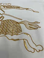 Close-up of gold embroidered horse graphic on a white long-sleeve shirt
