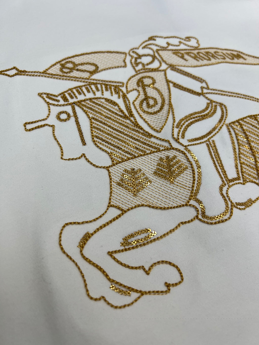 Close-up of gold embroidered horse-and-rider motif on a white shirt