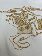 Close-up of gold embroidered horse-and-rider motif on a white shirt
