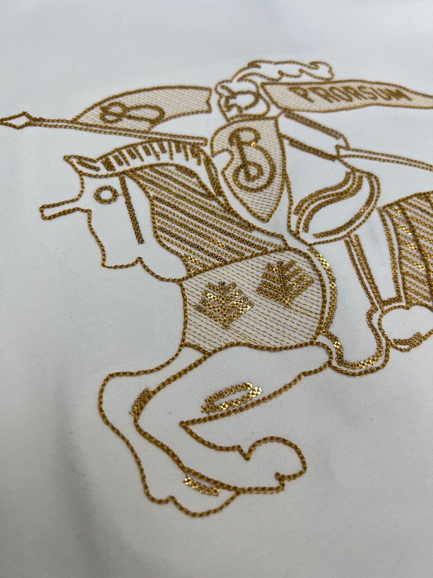 Close-up of gold embroidered horse-and-rider motif on a white shirt
