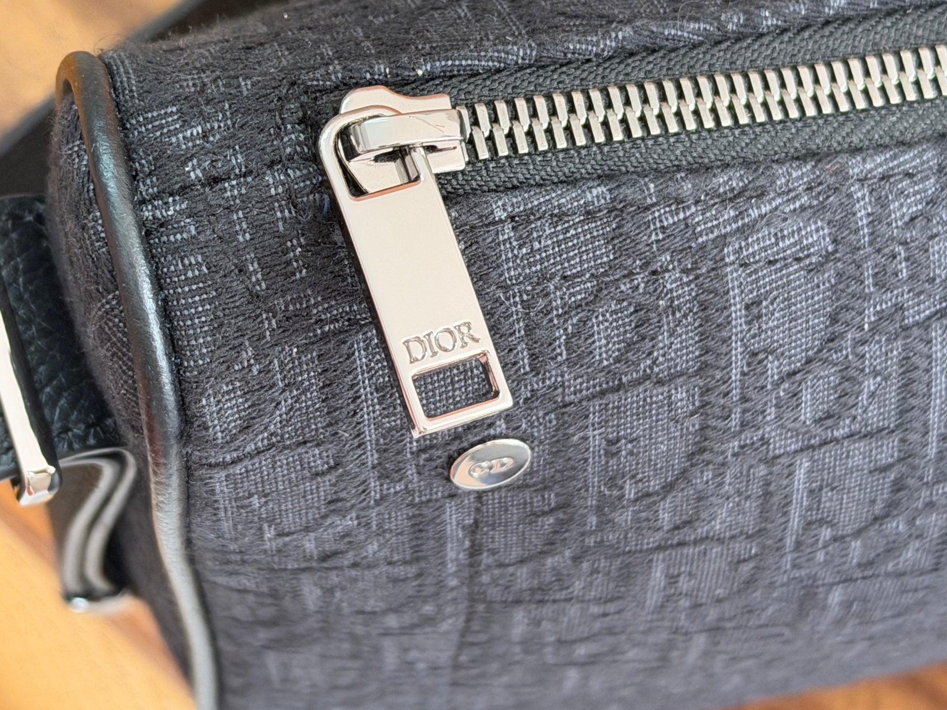 Dior logo zipper pull on dark blue fabric bag with silver hardware