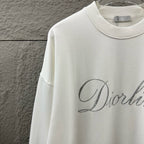 White long-sleeve sweatshirt with ribbed crew neck and partial glitter script logo.