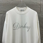 White long-sleeve sweatshirt close-up showing glitter “Diorling” script logo.