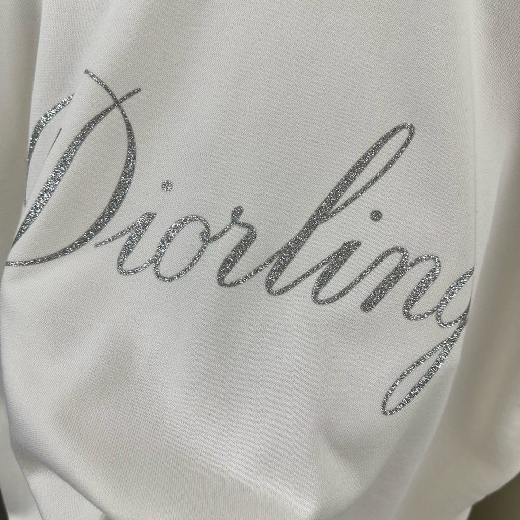 White sweatshirt close-up of glitter “Diorling” script across chest.
