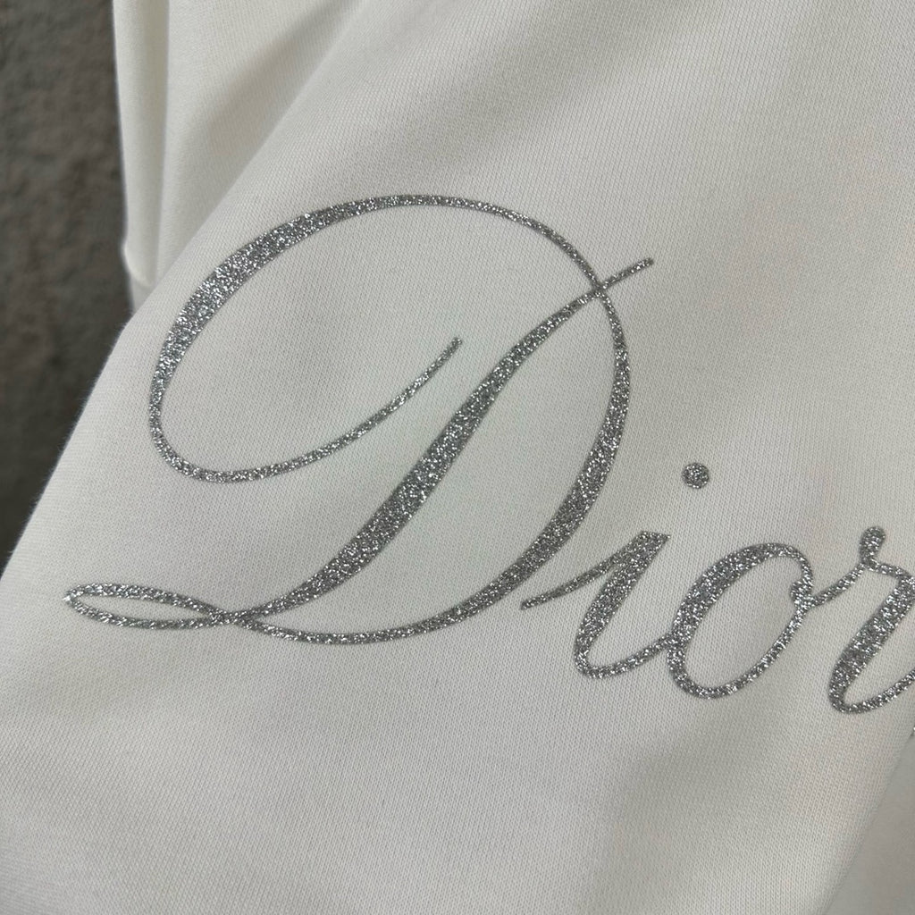 White sweatshirt close-up of large glitter “Diorling” script logo.