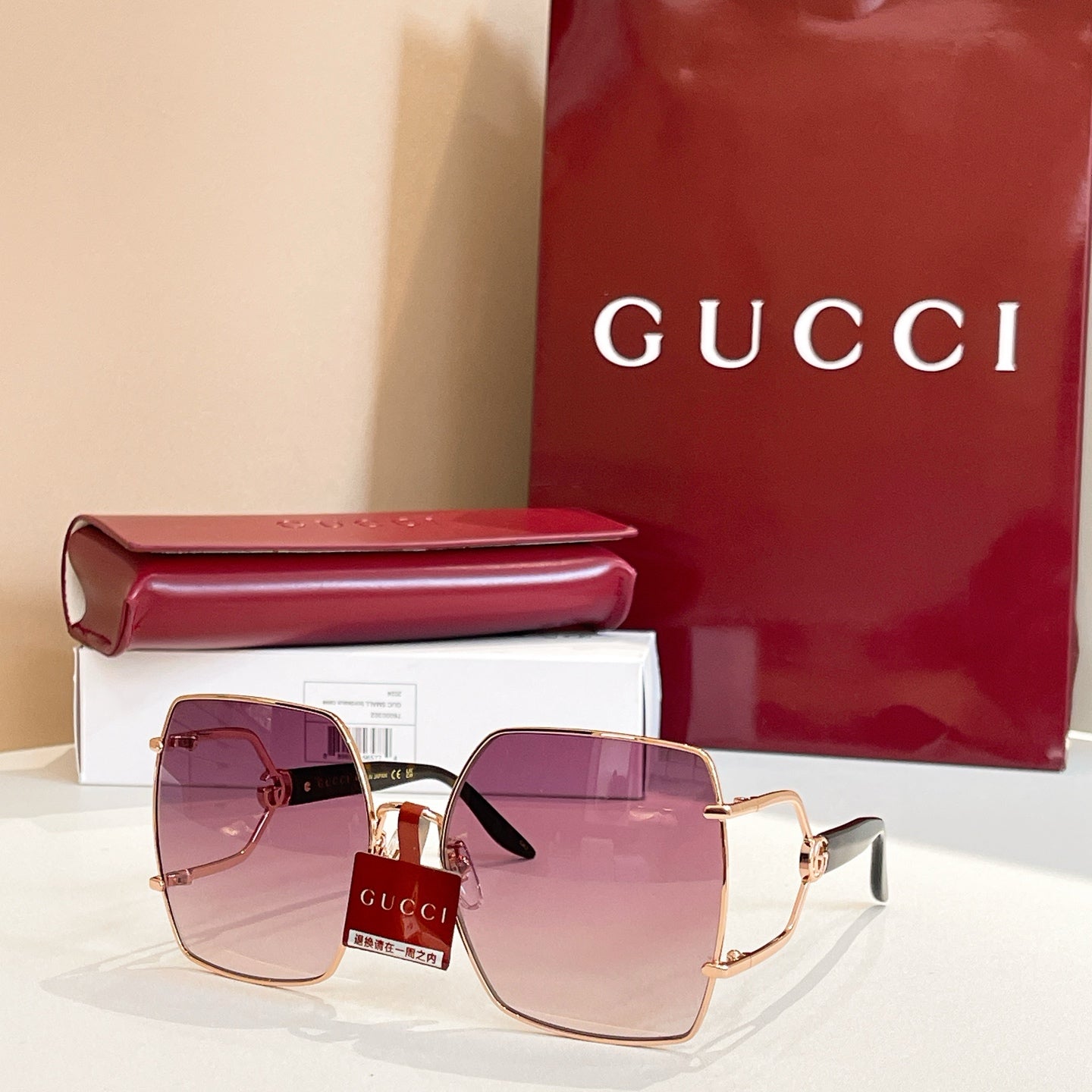 Square-edge sunglasses with rose-gold frame and mauve tinted lenses, front view with case.