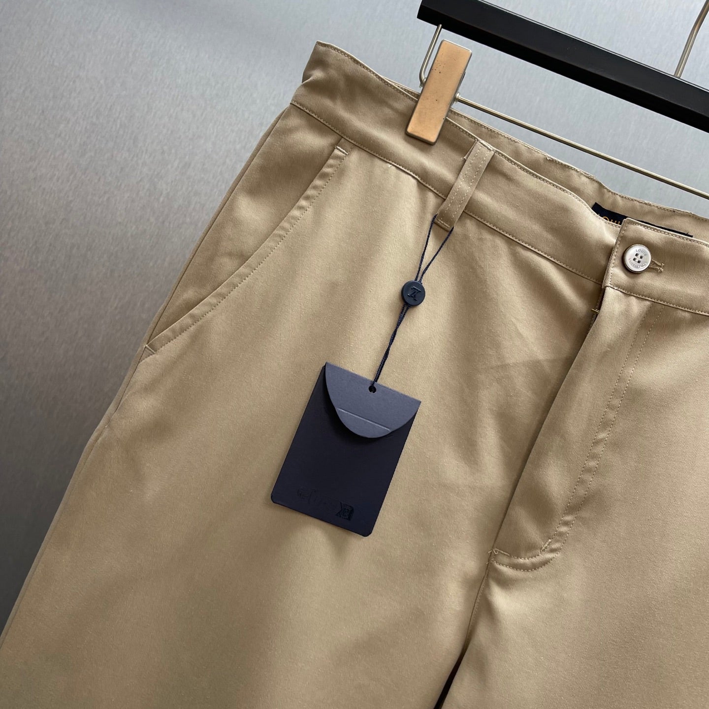 Louis Vuitton tan pants close-up at waistband with button and hanging tag