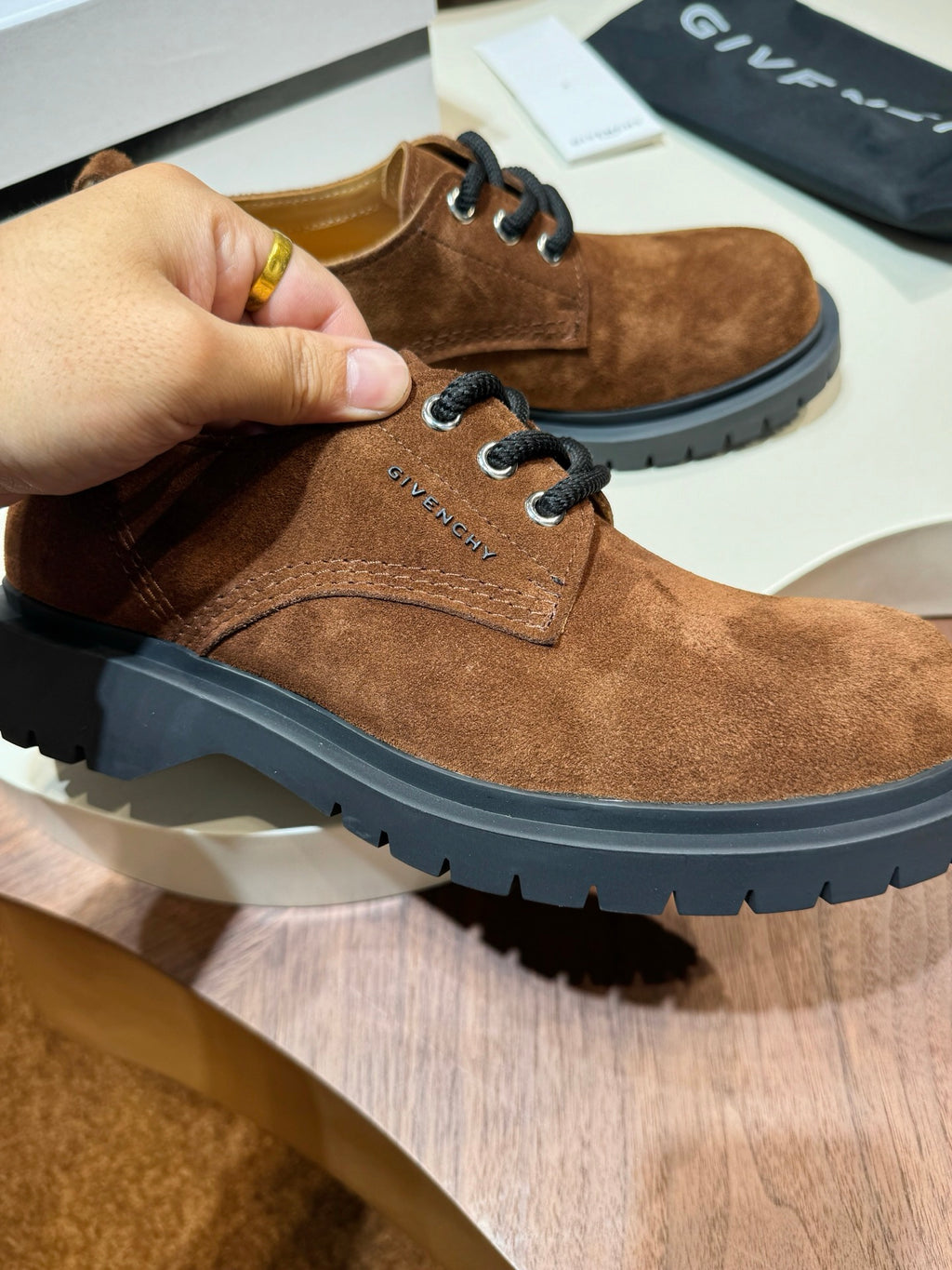 Brown suede lace-up shoe held by hand with black chunky sole and lace-up front