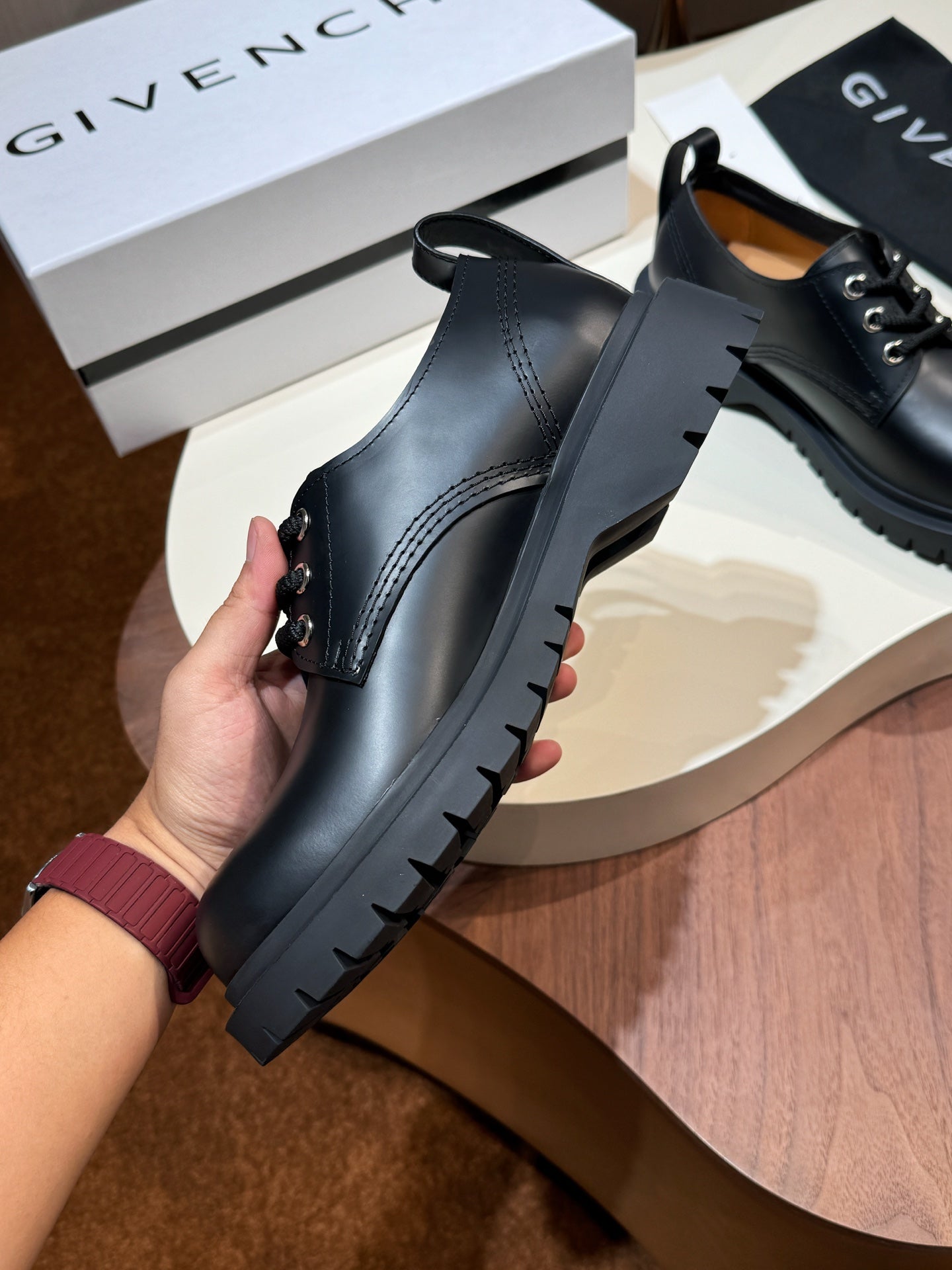 Black leather lace-up shoes with side stitching and chunky tread sole, hand-held