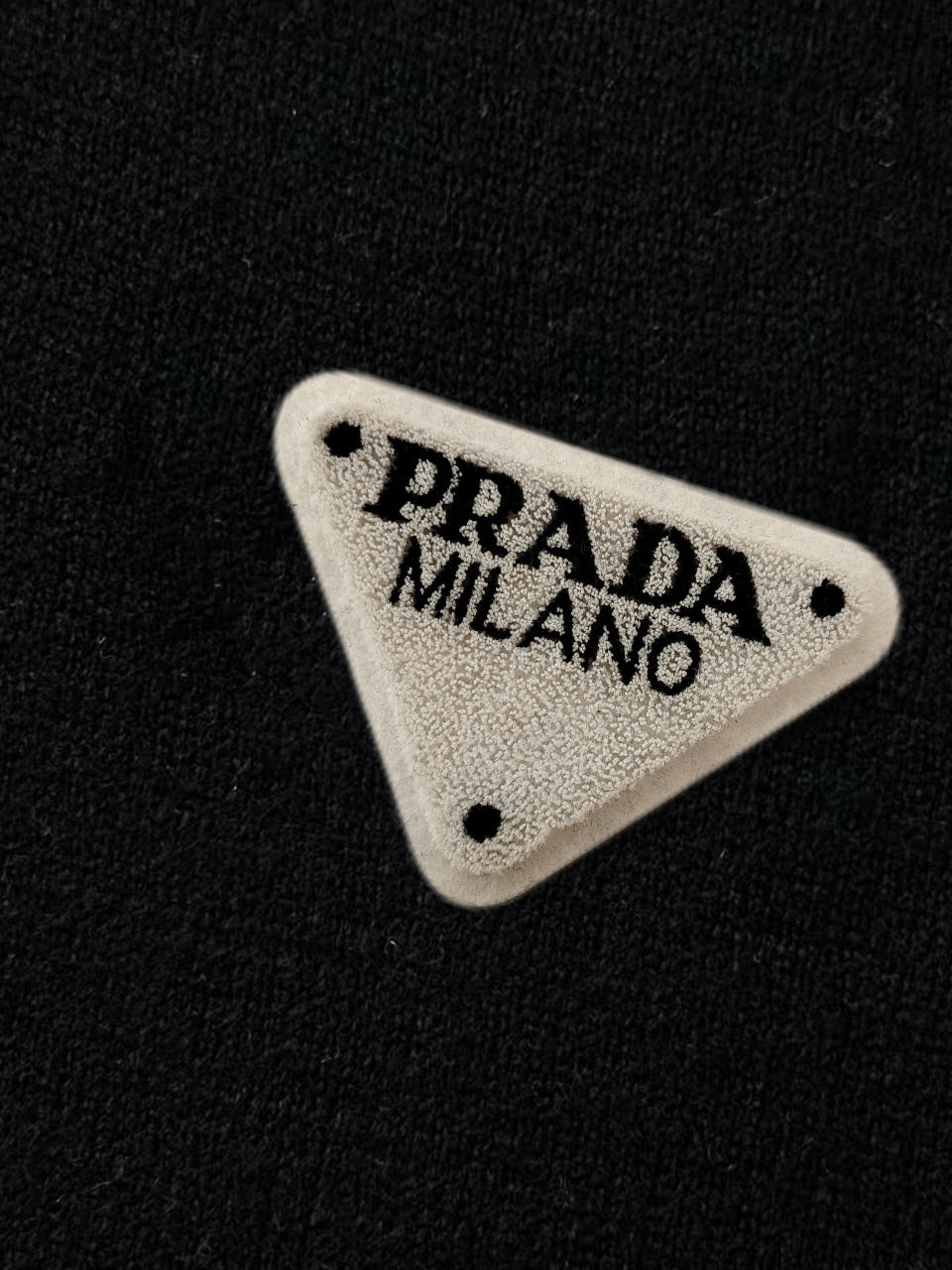 Triangular Prada Milano logo patch on black sweater fabric