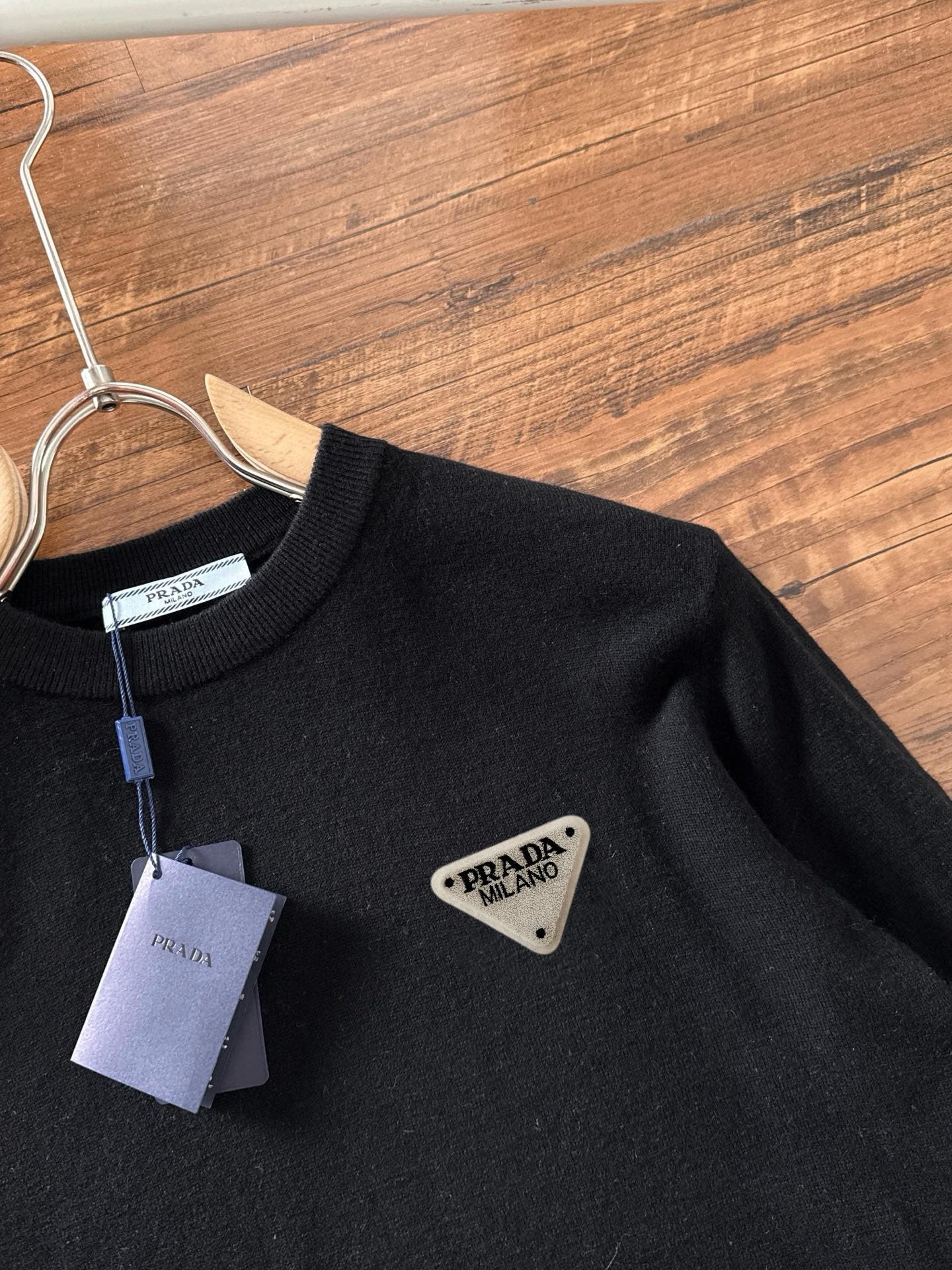 Black crewneck sweater with triangular Prada Milano logo patch on the chest