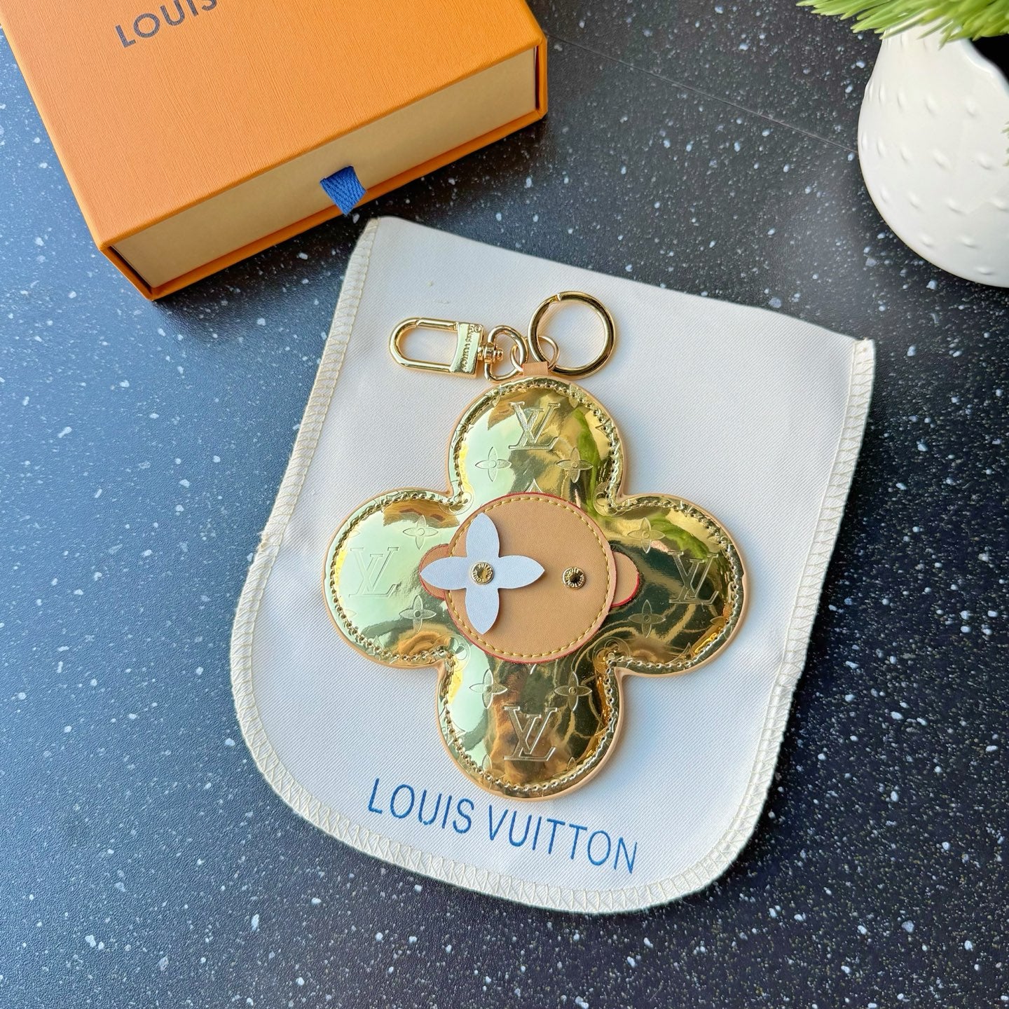 Louis Vuitton gold four-petal keychain charm with tan center and white flower detail