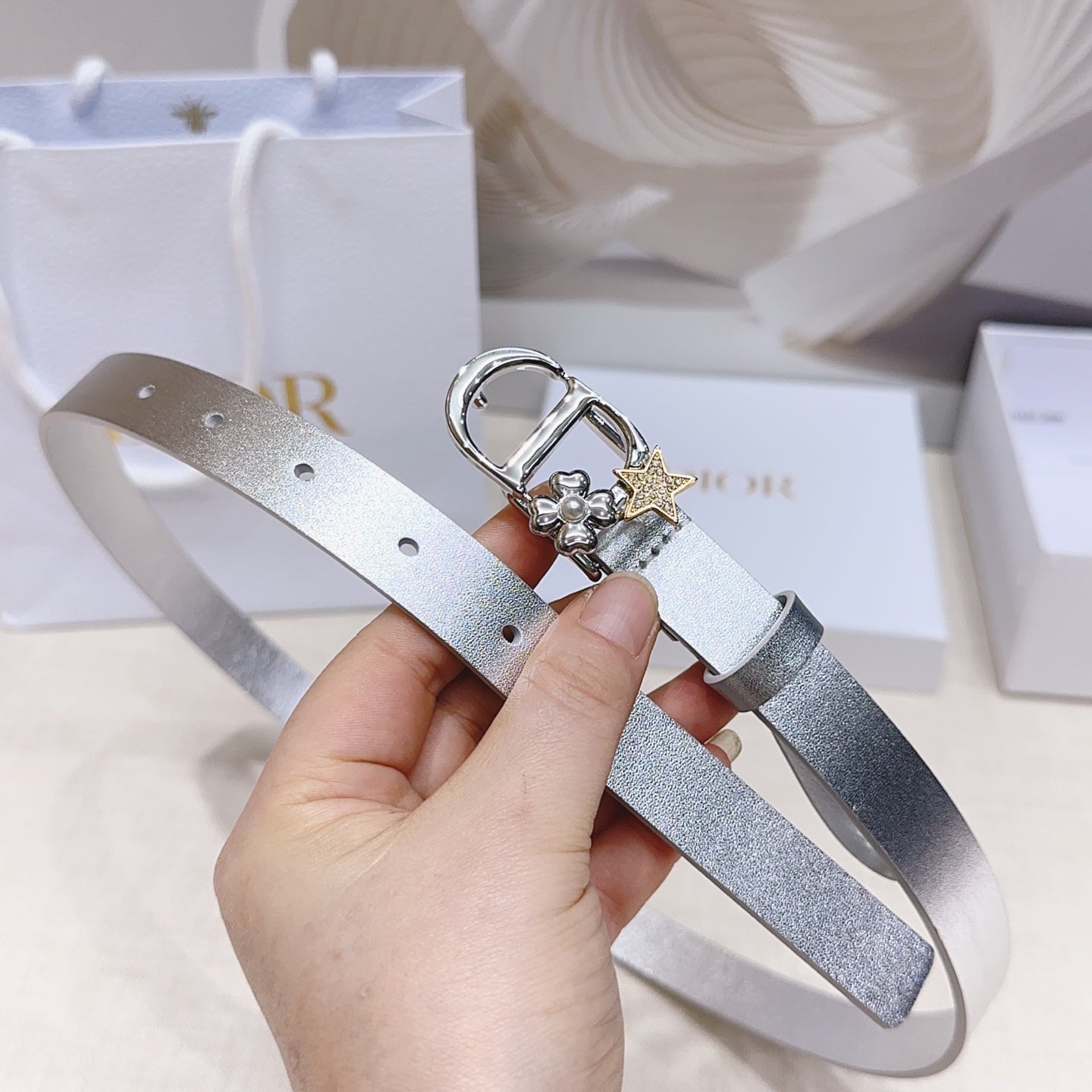 Silver metallic belt with oval buckle, star and flower charms, and eyelet holes
