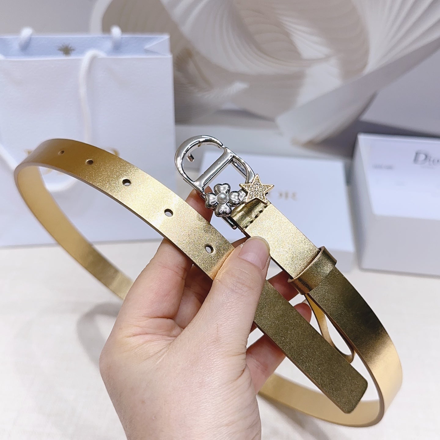 Dior belt with gold strap and silver buckle featuring floral detail and star charm.