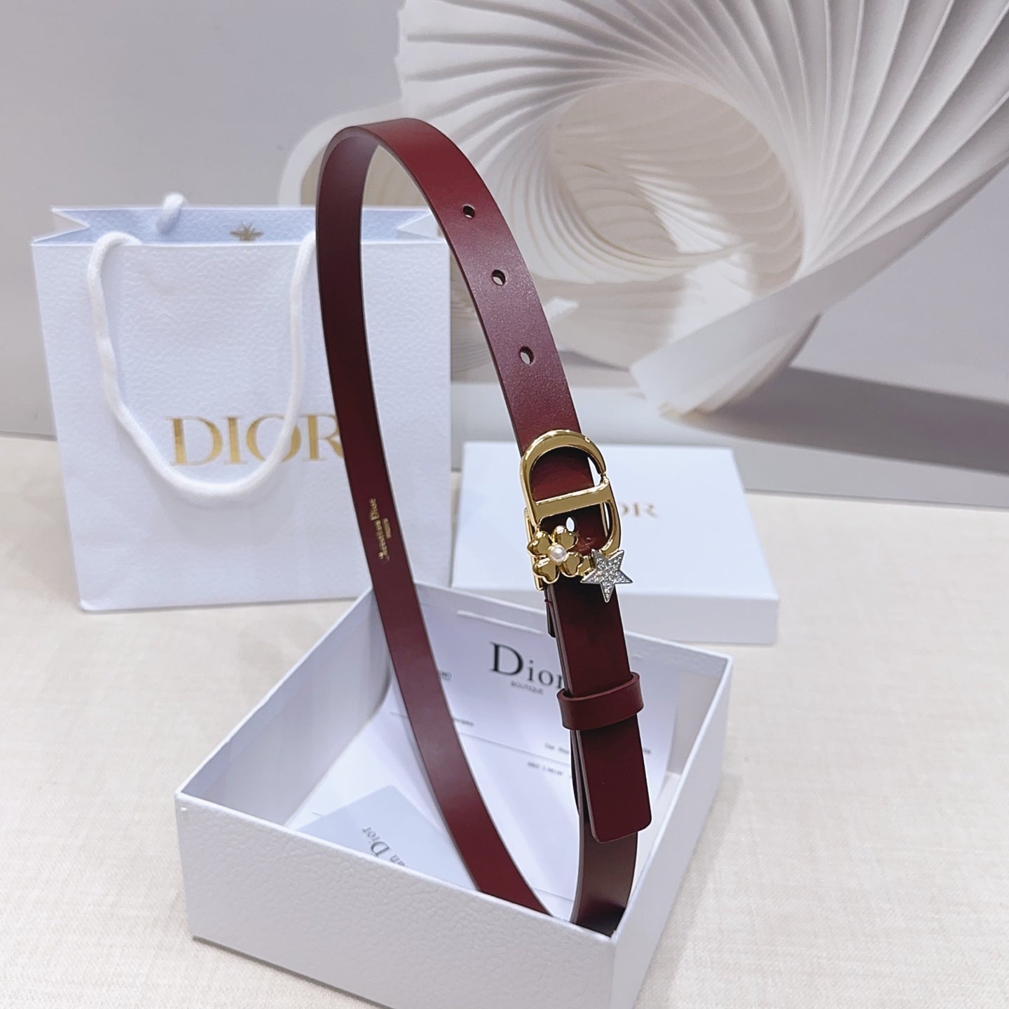 Dior burgundy belt with gold buckle and star charm on gift-box display