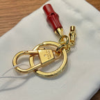 Gucci keychain close-up with gold clasp, red leather pull, on white pouch
