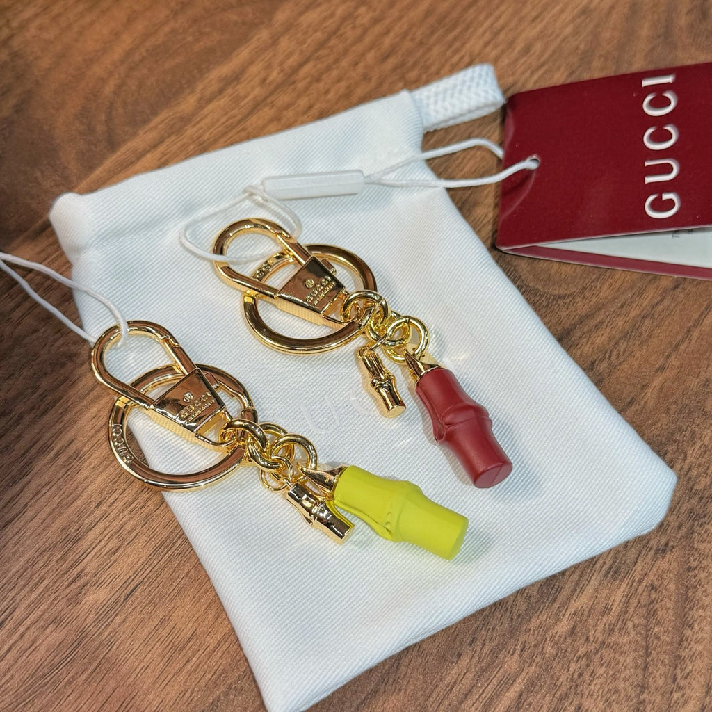 Gold-tone keychain pair with lime and red capsule charms in a white drawstring bag