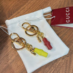 Gold-tone keychain pair with lime and red capsule charms in a white drawstring bag
